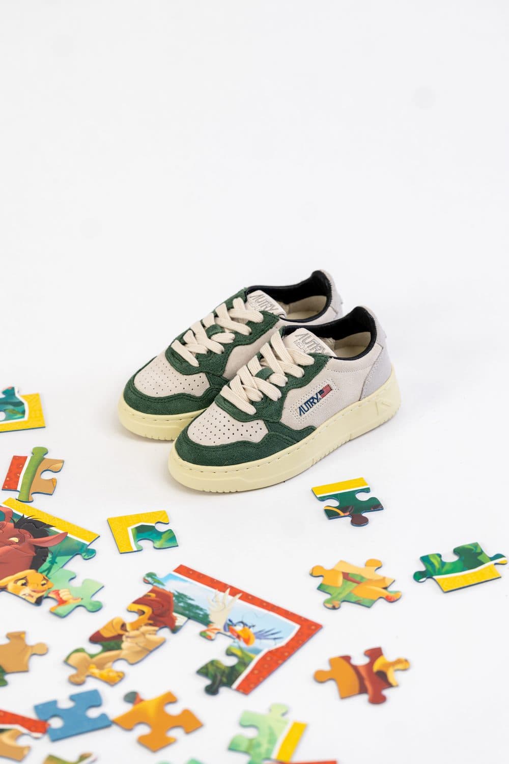 Shooting produit pour la boutique Contresens : baskets Autry enfant en daim vert et cuir blanc, entourées de pièces de puzzle