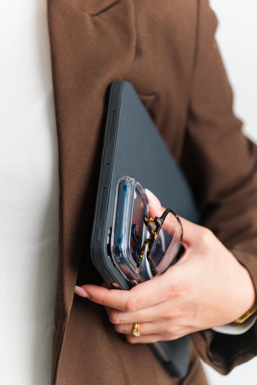 Détail : une main tient un téléphone et une tablette contre un blazer marron
